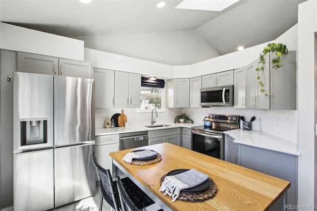 kitchen with decorative backsplash, lofted ceiling with skylight, a sink, appliances with stainless steel finishes, and gray cabinetry