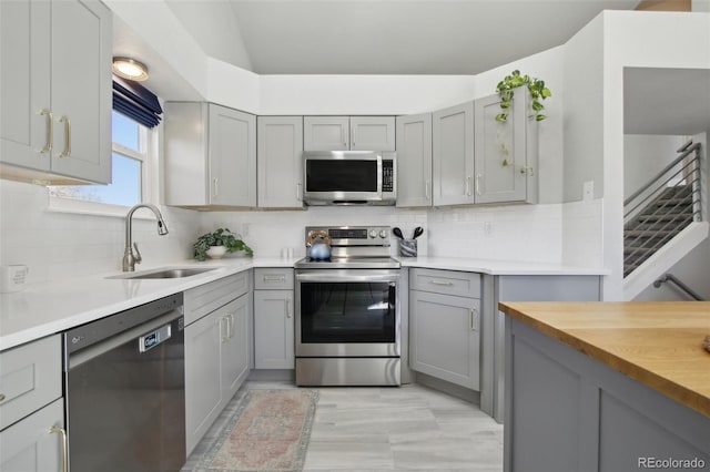 kitchen featuring a sink, decorative backsplash, appliances with stainless steel finishes, and gray cabinetry