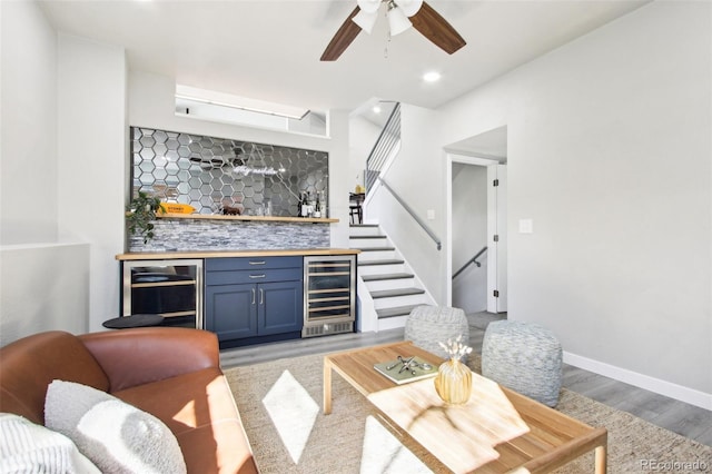 living room with light wood-style floors, a ceiling fan, indoor wet bar, wine cooler, and stairs