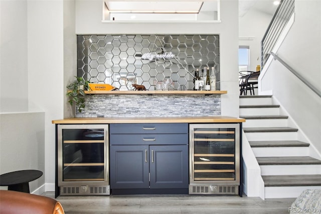 bar featuring a bar, wine cooler, wood finished floors, and stairway