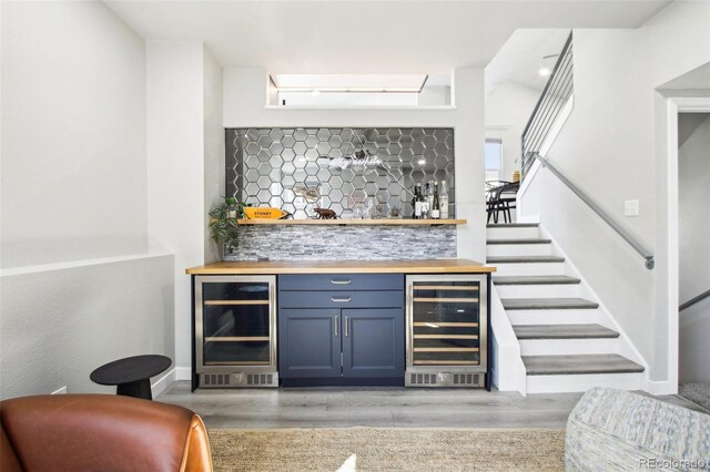 bar with wine cooler, a dry bar, and light wood-style flooring