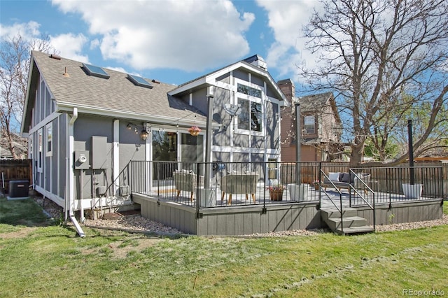 rear view of property featuring a deck, cooling unit, a chimney, a shingled roof, and a lawn