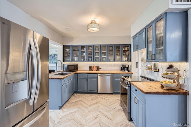 kitchen with stainless steel appliances, blue cabinetry, butcher block countertops, and a sink