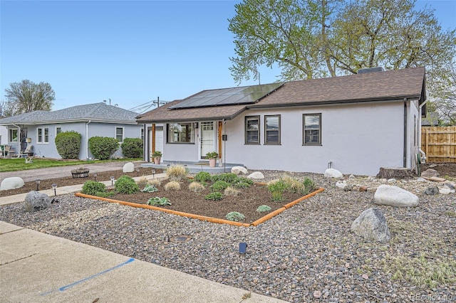 ranch-style home featuring fence, covered porch, roof with shingles, stucco siding, and roof mounted solar panels