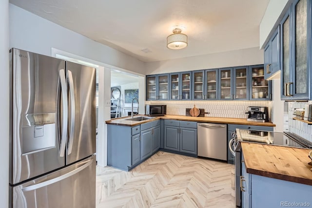 kitchen with a sink, wood counters, stainless steel appliances, and glass insert cabinets