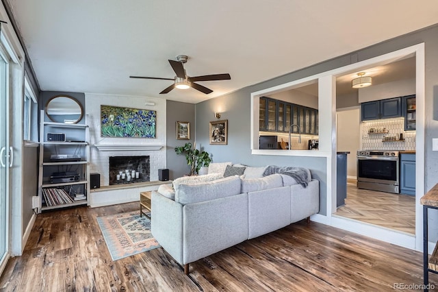 living room featuring a brick fireplace, dark wood-style floors, and ceiling fan