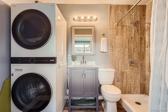 bathroom featuring vanity, toilet, wood finished floors, tiled shower, and stacked washer and clothes dryer