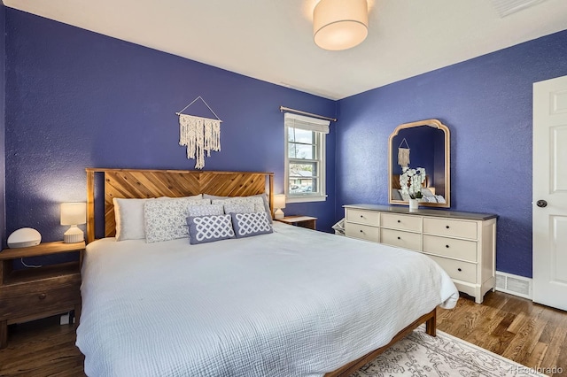 bedroom with visible vents, a textured wall, and wood finished floors