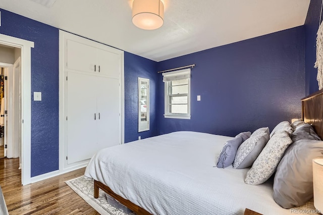 bedroom with baseboards, a textured wall, a closet, and wood finished floors