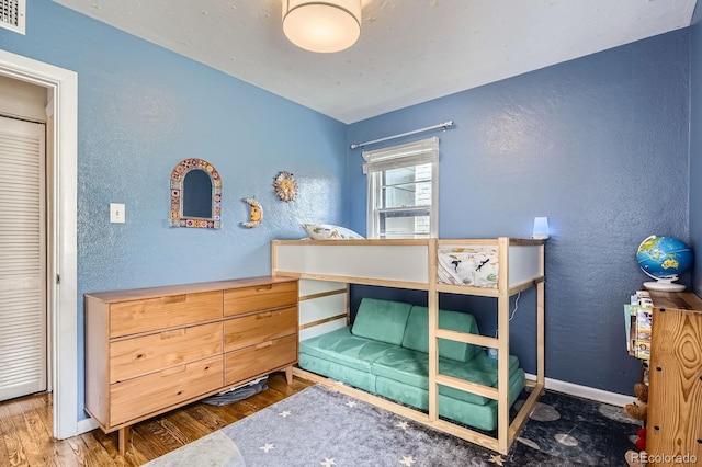 bedroom featuring a textured wall, visible vents, baseboards, and wood finished floors
