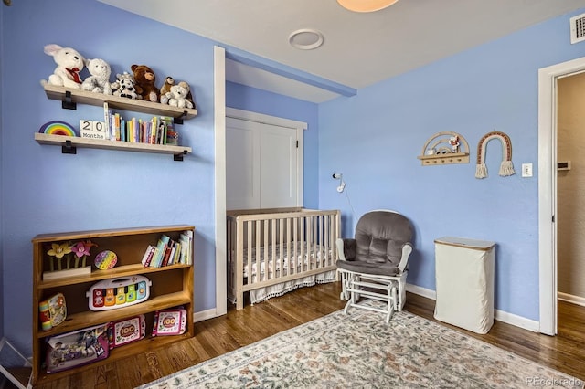 bedroom featuring baseboards, a crib, wood finished floors, and visible vents