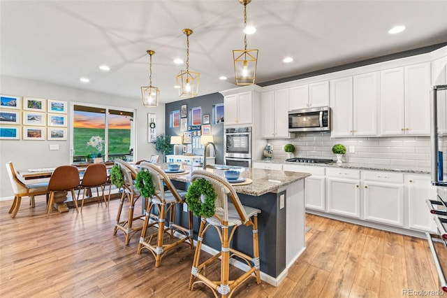17335 W 94th Ave, Arvada, CO 80007 - kitchen with appliances with stainless steel finishes, recessed lighting, light wood-style floors, a breakfast bar, and a kitchen island with sink