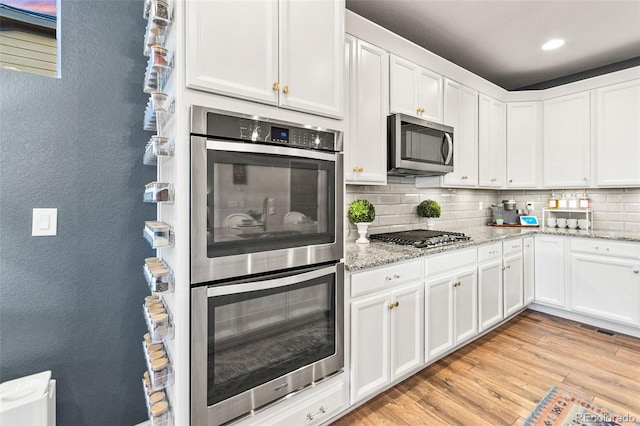 17335 W 94th Ave, Arvada, CO 80007 - kitchen with stainless steel appliances, white cabinetry, tasteful backsplash, a textured wall, and light wood-type flooring