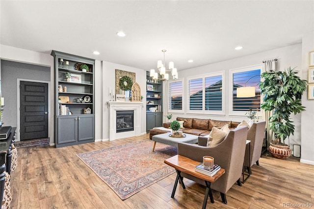 17335 W 94th Ave, Arvada, CO 80007 - living area featuring wood finished floors, a chandelier, a glass covered fireplace, recessed lighting, and built in shelves