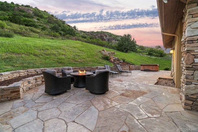 patio terrace at dusk with a yard, a jacuzzi, and a fire pit