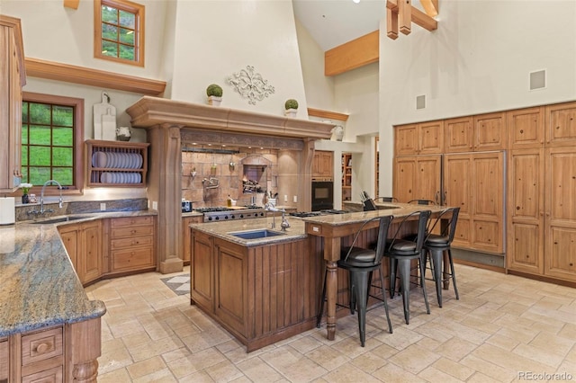 kitchen with stone counters, a breakfast bar, an island with sink, a high ceiling, and exhaust hood