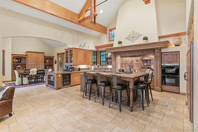 kitchen with black double oven, high vaulted ceiling, beverage cooler, and a kitchen breakfast bar