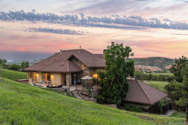 back house at dusk featuring a patio, a mountain view, and a lawn