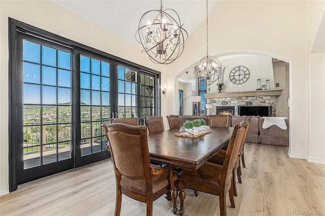 12963 Silver Elk Ln, Littleton, CO 80127 - dining area featuring a chandelier, arched walkways, light wood-style flooring, a high ceiling, and a stone fireplace