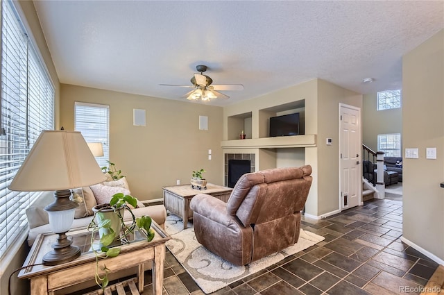 living room featuring ceiling fan, a fireplace, a textured ceiling, stairs, and baseboards