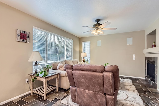 living room with ceiling fan, a tiled fireplace, and baseboards