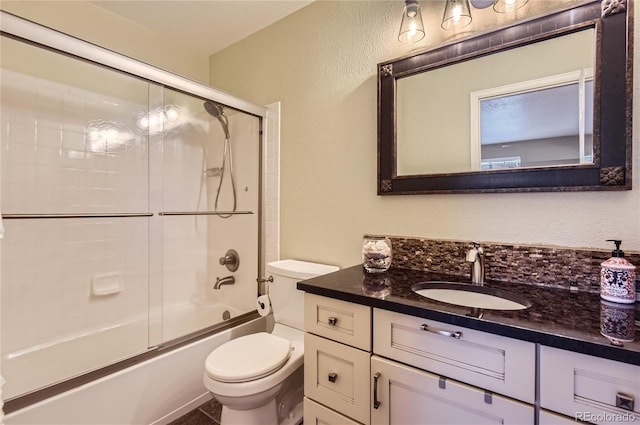 bathroom featuring vanity, a textured wall, combined bath / shower with glass door, and toilet