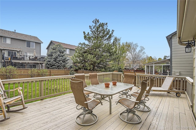 deck with outdoor dining area, a fenced backyard, and a lawn