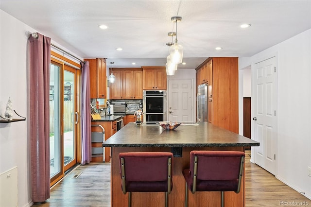 10378 W Weaver Ave, Littleton, CO 80127 - kitchen with appliances with stainless steel finishes, dark countertops, light wood-type flooring, a kitchen island, and recessed lighting