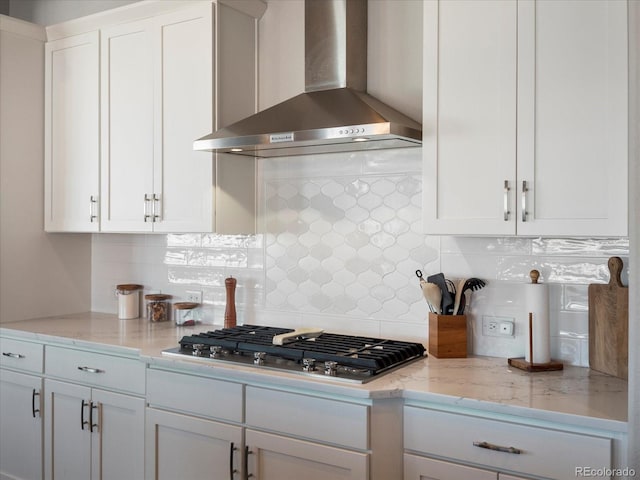 kitchen featuring wall chimney range hood, decorative backsplash, stainless steel gas cooktop, and white cabinets