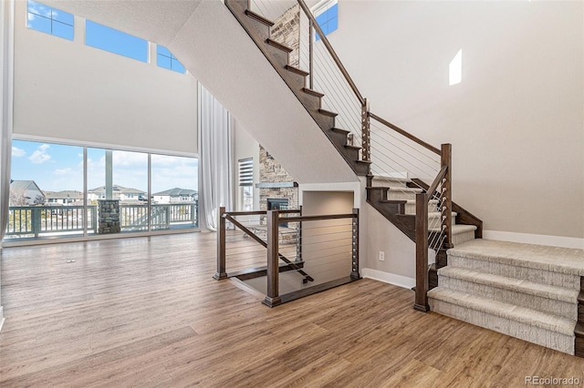 staircase with hardwood / wood-style flooring, a towering ceiling, and a stone fireplace