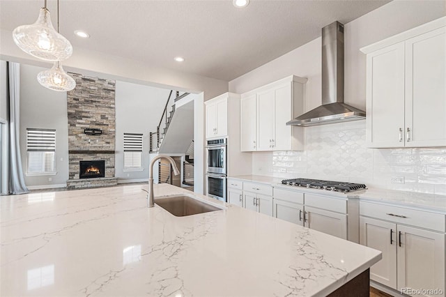 kitchen featuring sink, decorative light fixtures, wall chimney range hood, stainless steel appliances, and white cabinets