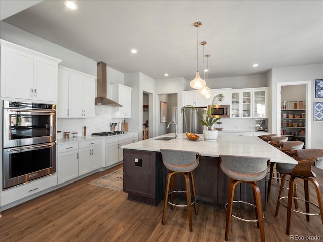 kitchen with appliances with stainless steel finishes, white cabinetry, sink, a large island, and wall chimney exhaust hood