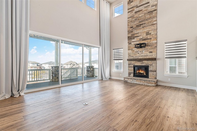 unfurnished living room with hardwood / wood-style flooring, a stone fireplace, and a high ceiling