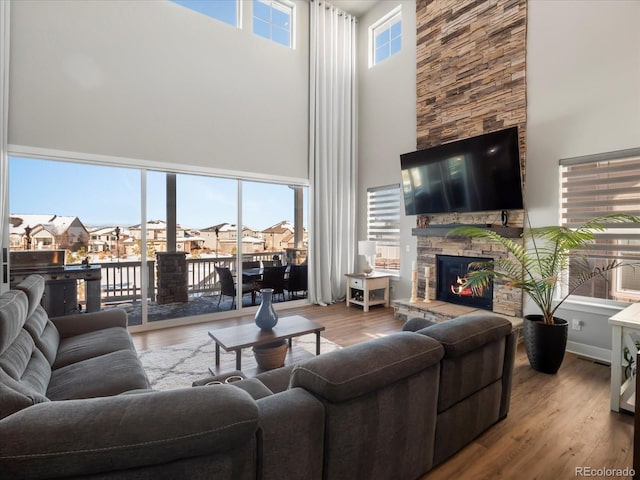 living room featuring a stone fireplace, plenty of natural light, wood-type flooring, and a high ceiling