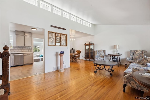 living area with light wood-style flooring, a chandelier, plenty of natural light, and a towering ceiling