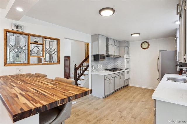 kitchen with light wood finished floors, a sink, gray cabinets, visible vents, and tasteful backsplash