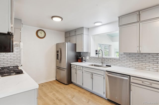 kitchen with a sink, tasteful backsplash, gray cabinets, light wood finished floors, and appliances with stainless steel finishes