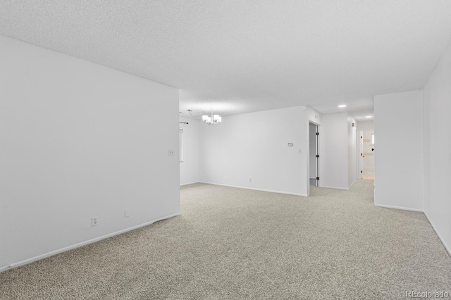 carpeted empty room featuring a notable chandelier and a textured ceiling