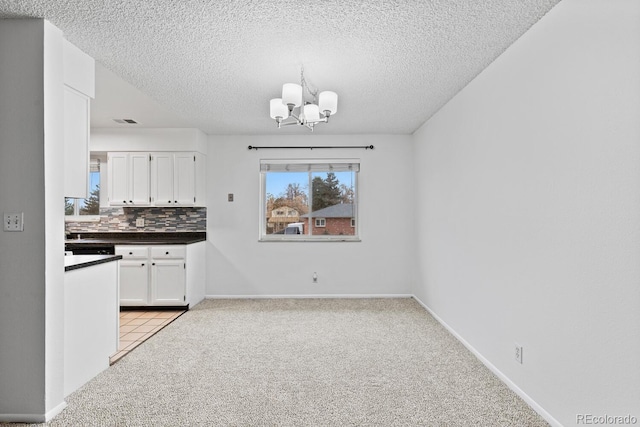 unfurnished dining area featuring light carpet, a textured ceiling, and a notable chandelier