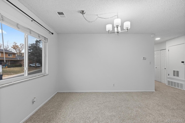 carpeted spare room featuring a textured ceiling and a notable chandelier