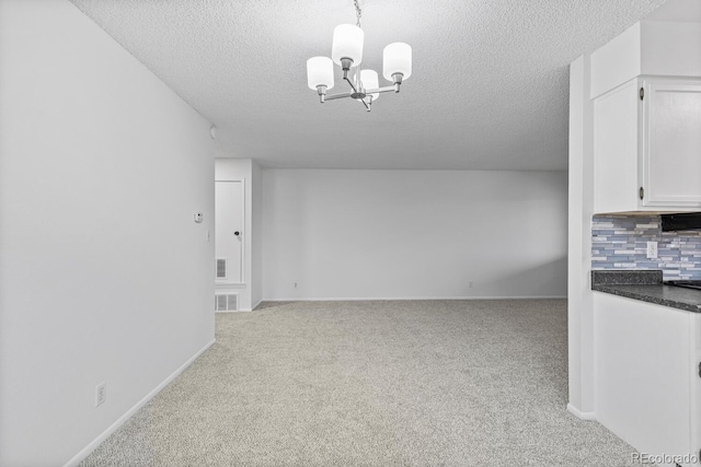 unfurnished dining area with light colored carpet, a textured ceiling, and a notable chandelier