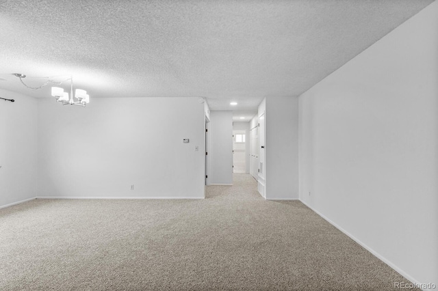 empty room with a textured ceiling, light carpet, and an inviting chandelier