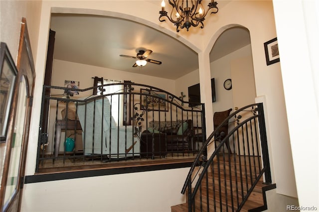 staircase with arched walkways and ceiling fan with notable chandelier