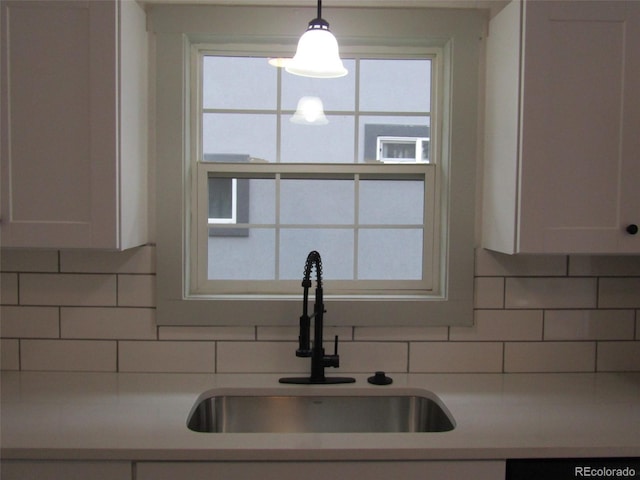 kitchen featuring decorative backsplash, white cabinetry, sink, and hanging light fixtures