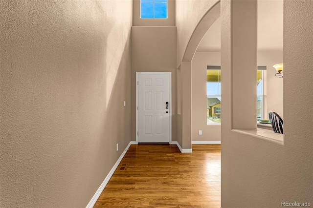 foyer entrance featuring wood finished floors, arched walkways, a high ceiling, baseboards, and a textured wall