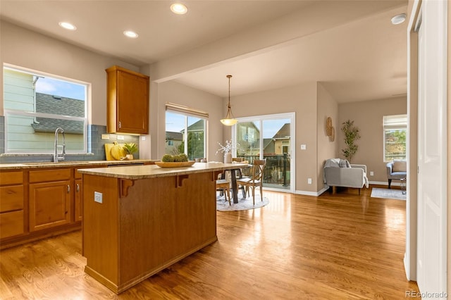 kitchen with light wood-type flooring, a sink, plenty of natural light, a kitchen island, and backsplash