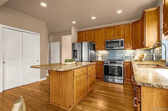 kitchen featuring a sink, wood finished floors, a center island, stainless steel appliances, and decorative backsplash