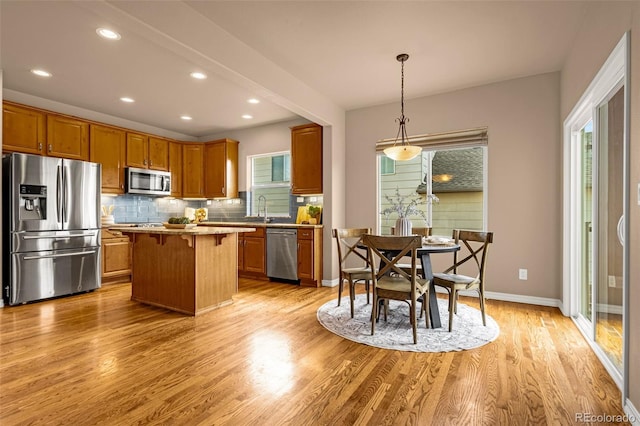 kitchen featuring a sink, tasteful backsplash, a kitchen island, light wood-style floors, and appliances with stainless steel finishes