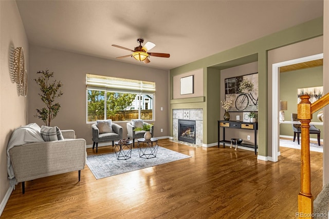 living area featuring baseboards, a ceiling fan, wood finished floors, and a fireplace