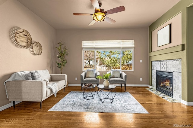 living area with baseboards, a fireplace, wood finished floors, and a ceiling fan